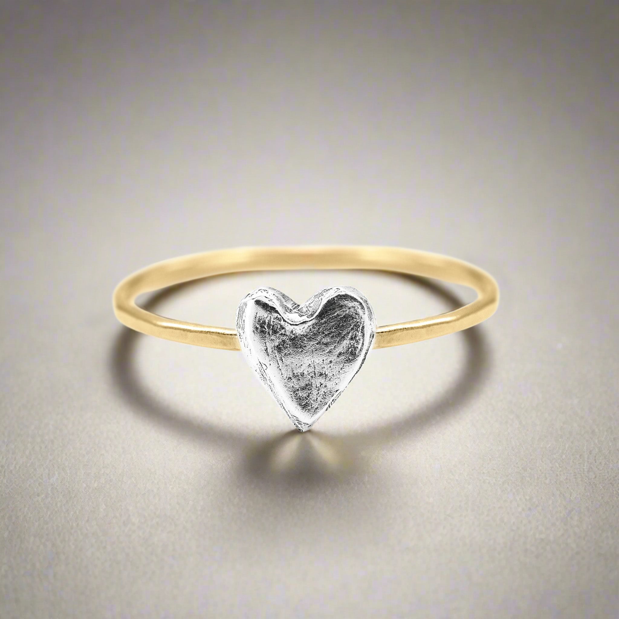 Gold ring with a silver heart-shaped pendant on a neutral background